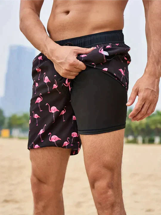 Mann in Flamingo-Badeshorts am Strand, schwarz-rosa, Sommermode, Herrenbekleidung.