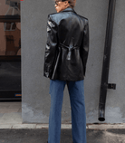 Frau in schwarzer Lederjacke und Vintage-Jeans mit niedriger Taille, steht vor grauer Wand. Modetrend, Streetstyle, Herbstmode.
