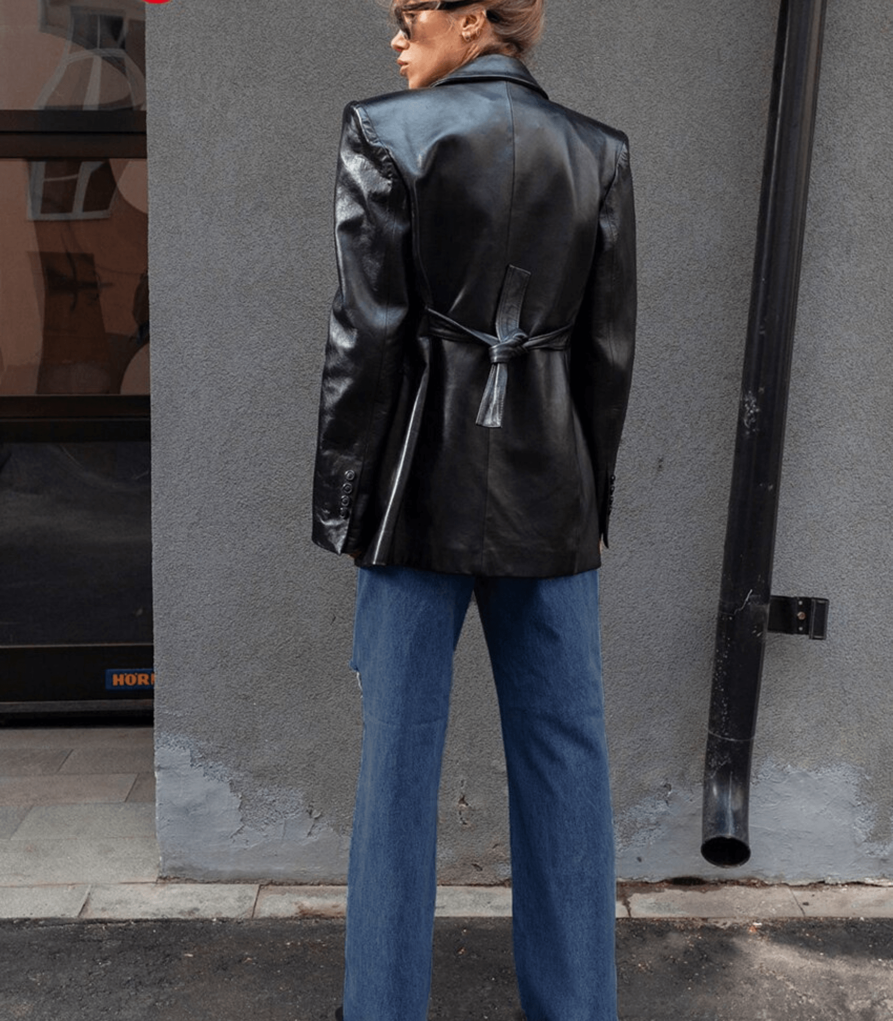 Frau in schwarzer Lederjacke und Vintage-Jeans mit niedriger Taille, steht vor grauer Wand. Modetrend, Streetstyle, Herbstmode.