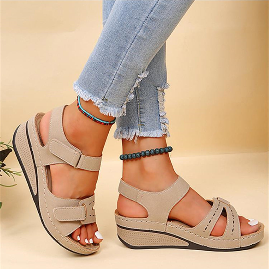 Beige Sandalen mit Keilabsatz, Klettverschluss und perforiertem Design, kombiniert mit modischen, zerrissenen Jeans. Ideal für Sommermode.