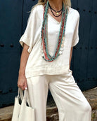 Frau in weißem Leinen-Outfit mit bunten Halsketten, modisch, elegant, Sommermode, Accessoires, lässiger Stil, Damenbekleidung, Trend 2023.