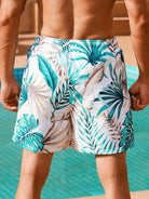 Herren-Badeshorts mit tropischem Blattmuster, grün-weiß, am Pool, Sommermode.
