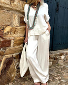 Elegantes Damen-Outfit in Weiß mit lässiger Bluse und weiter Hose, ergänzt durch lange Halsketten. Perfekt für Sommermode und Boho-Stil.