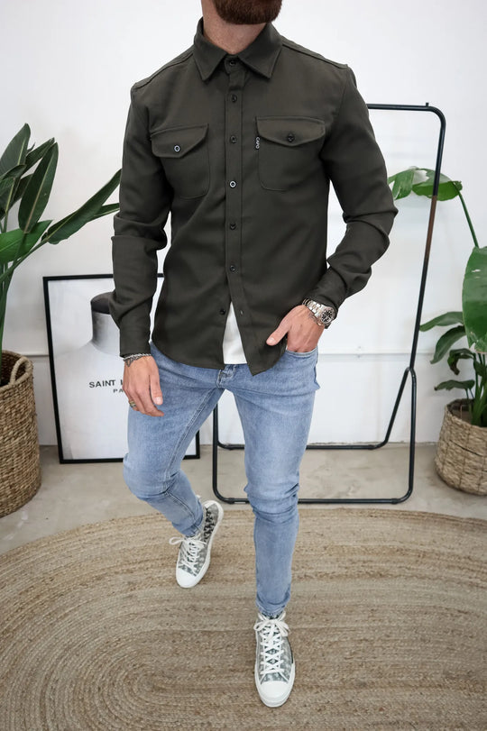 Mann in olivgrünem Hemd und blauer Jeans, lässiger Stil, moderne Herrenmode, Streetwear, stilvolle Freizeitkleidung, trendige Outfits.