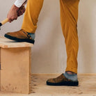 Person in gelber Hose und braunen Schuhen bearbeitet Holz mit einem Hammer. Handwerk, DIY, Holzarbeit, Heimwerker, Werkzeuge.