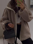 Damenmode: Flauschige Teddyjacke in Beige, kombiniert mit schwarzer Mini-Handtasche. Trendige Winterbekleidung, stilvoll und warm.