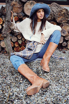 Frau in lässiger Herbstmode: blauer Hut, cremefarbener Pullover, Jeans, braune Stiefel. Perfekt für Outdoor-Abenteuer und modische Herbstlooks.
