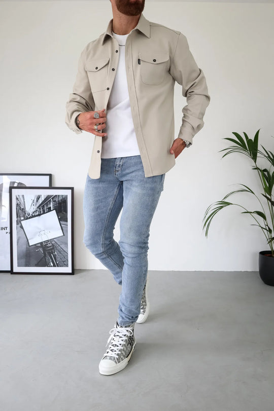 Moderner Mann in beiger Hemdjacke, weißem T-Shirt und blauen Jeans. Stilvolle Sneaker, lässiger Look. Herrenmode, Freizeitkleidung, Trend.