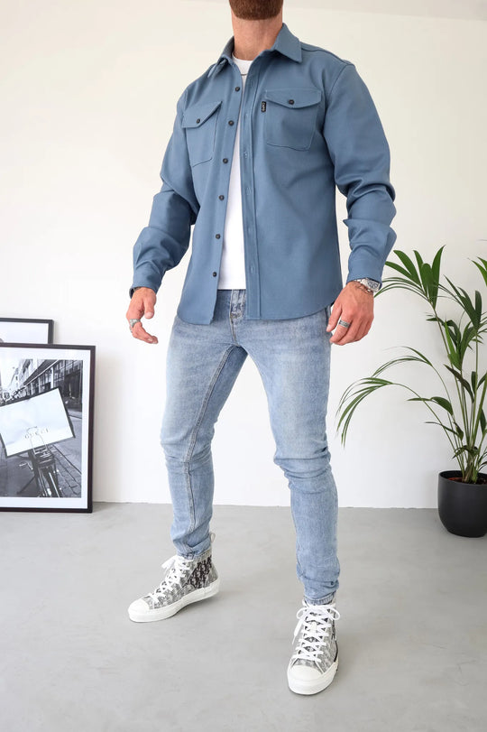Mann in blauer Hemdjacke, hellen Jeans und bedruckten Sneakers. Modetrend, Herrenmode, lässiger Stil, Streetwear, Outfit-Inspiration.