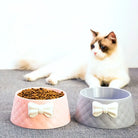 Rosa und graue Katzennäpfe mit Schleifen-Design, gefüllt mit Trockenfutter, vor einer flauschigen Katze. Perfekt für stilvolle Haustierfütterung.