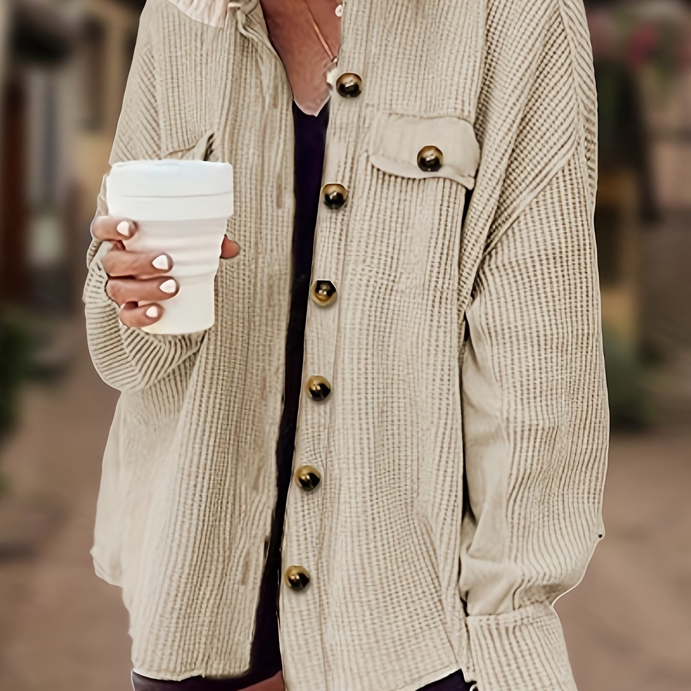 Frau in beiger Strickjacke mit großen Knöpfen hält einen weißen Kaffeebecher. Modetrend, Herbstmode, lässiger Stil, Damenbekleidung.