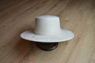 Breiter cremefarbener Filzhut auf Holzboden, stilvoll und zeitlos. Perfekt für Mode, Accessoires, Cowboyhut, Westernstil, Unisex.