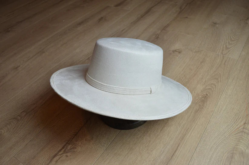 Eleganter weißer Filzhut mit breiter Krempe auf Holzboden. Perfekt für stilvolle Outfits, modische Accessoires, zeitloses Design.