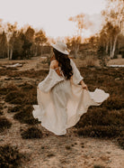 Frau in weißem Boho-Kleid und Hut in herbstlicher Landschaft. Boho-Mode, Herbstkleidung, Natur, stilvolle Damenmode, Outdoor-Fotografie.