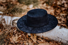 Schwarzer Filzhut auf Birkenstamm im Herbstlaub. Eleganter, zeitloser Hut, ideal für Herbstmode. Perfekt für stilvolle Outdoor-Looks.