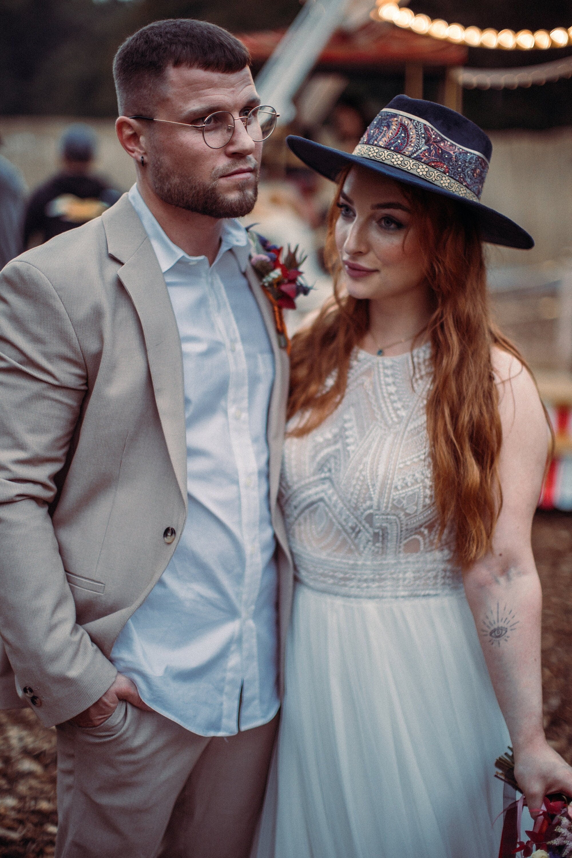 Brautpaar im Boho-Stil: Braut in Spitzenkleid, Bräutigam im beigen Anzug. Hochzeit, Boho-Chic, Vintage, romantisch, Outdoor-Event.