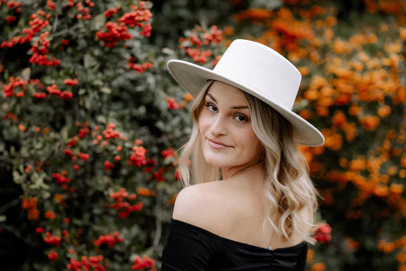 Frau mit weißem Hut vor herbstlicher Kulisse aus roten und orangefarbenen Beeren. Mode, Herbst, Natur, stilvoll, Outdoor-Porträt.