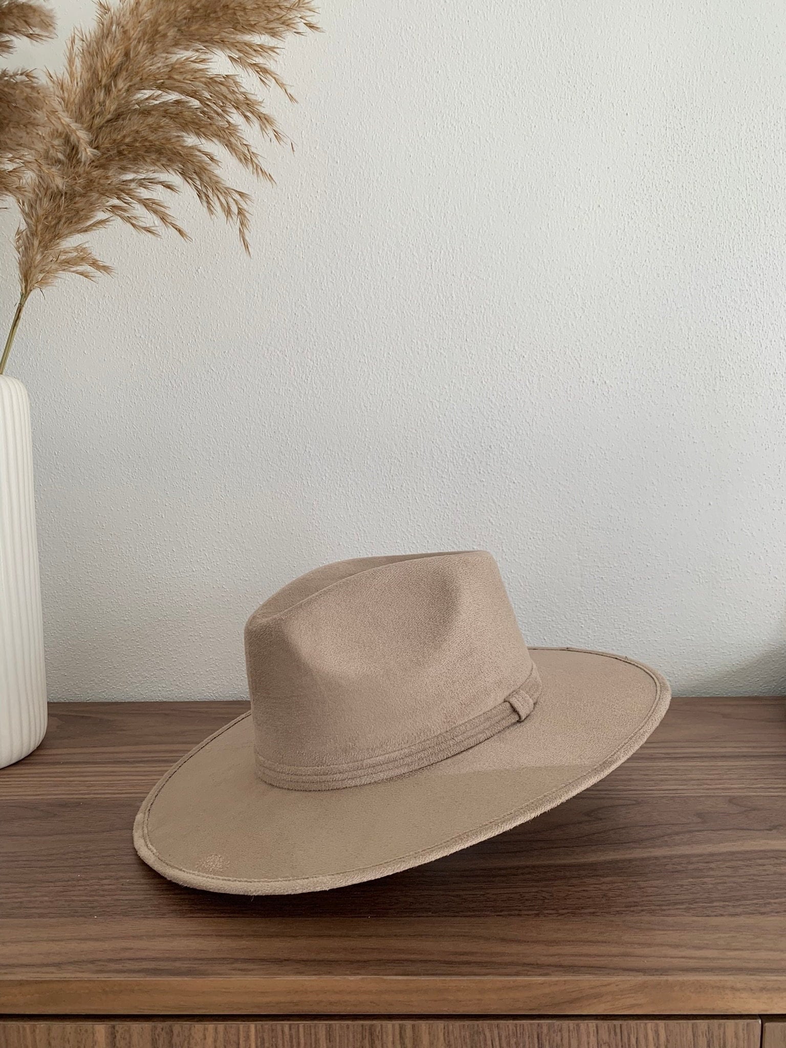 Beiger Fedora-Hut aus Filz auf Holztisch, minimalistische Dekoration, stilvoller Kopfschmuck, ideal für Mode und Accessoires.