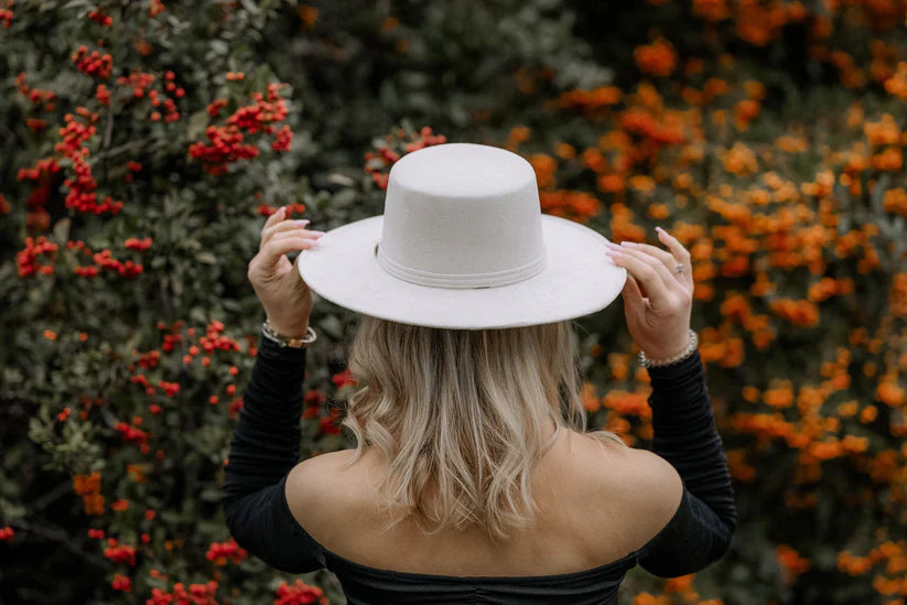 Frau mit weißem Hut vor herbstlicher Kulisse aus roten und orangefarbenen Beeren. Mode, Herbst, Natur, stilvoll, Outdoor-Fotografie.
