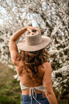 Frau mit Strohhut vor blühenden Kirschbäumen, Rückenansicht. Frühling, Natur, Mode, Outdoor, Blumen, Jeans, Strohhut, romantische Atmosphäre.