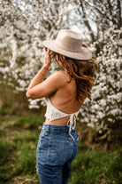 Frau in Jeans und gehäkeltem Top vor blühenden Bäumen, trägt Hut. Frühling, Mode, Natur, Outdoor, lässiger Stil, Boho-Chic, Damenbekleidung.