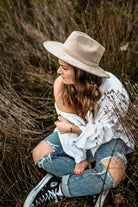 Frau in zerrissenen Jeans und weißem Hemd, sitzt im Gras, trägt beigen Hut. Lässiger Boho-Stil, Natur, Modefotografie, Outdoor-Porträt.