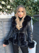 Frau in schwarzer Lederjacke mit Pelzkragen, blondes Haar, vor Holzwand mit Efeu und weißen Rosen. Modetrend, Wintermode, stilvoll.