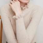 Damenpullover aus beigem Strick mit Rüschenkragen und -ärmeln, elegant und modisch, ideal für Herbstmode. Hochwertige Strickware.