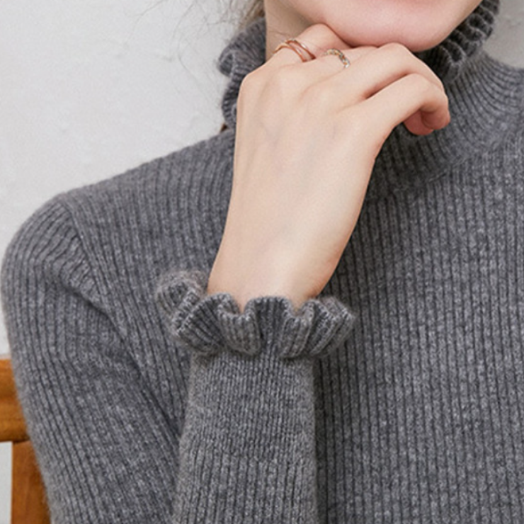 Grauer Rollkragenpullover aus Strick mit Rüschenärmeln, elegant und warm, ideal für Herbstmode. Damenmode, Strickpullover, Rollkragen.