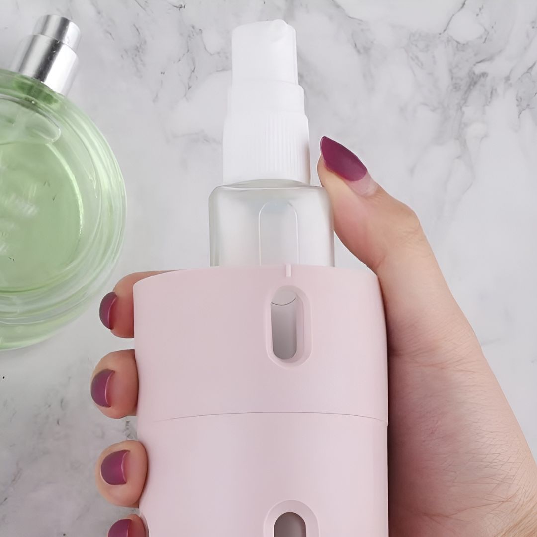 Hand hält rosa Sprühflasche auf Marmorhintergrund, Parfümflakon daneben.