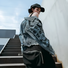 Frau in zerrissener Jeansjacke mit Graffiti-Design, schwarze Kappe, urbaner Stil, Streetwear, Treppe, modisch, trendig, lässig, Outdoor.