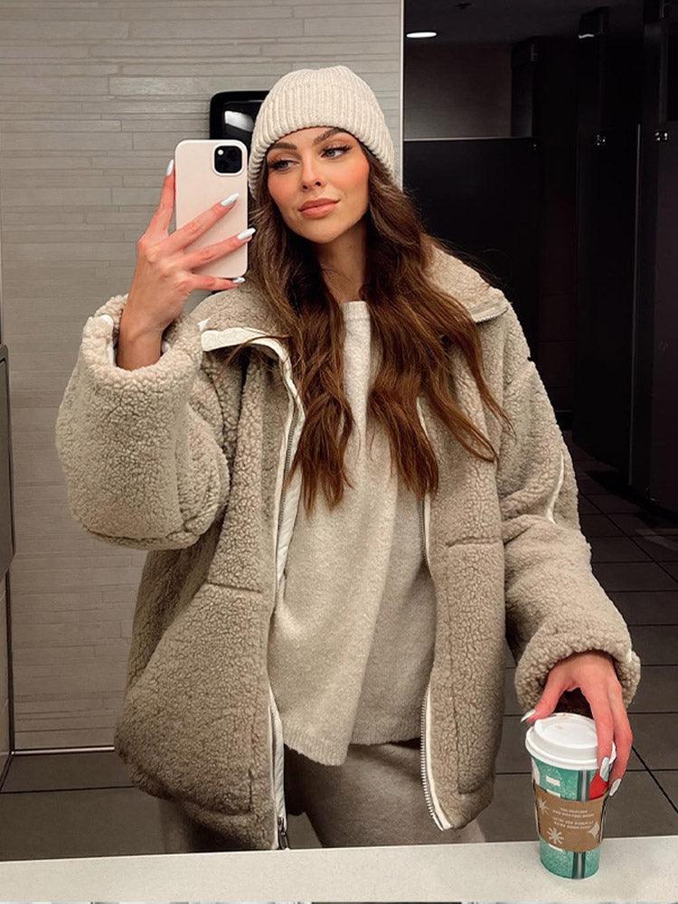 Frau in beiger Teddyjacke und Mütze macht Selfie im Spiegel, hält Starbucks-Becher. Wintermode, gemütlicher Look, trendige Outfits.