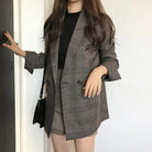 Frau in kariertem Blazer, schwarzem Top und beiger Hose. Modetrend, Business-Look, eleganter Stil, Damenmode, Herbstmode, Blazer-Outfit.