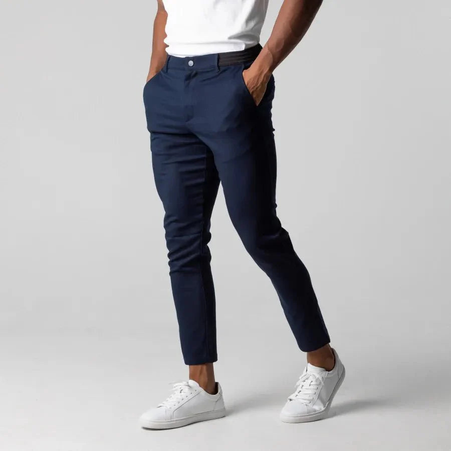 Mann trägt dunkelblaue Chinohose, weiße Sneaker, weißes T-Shirt, modisch, lässig.