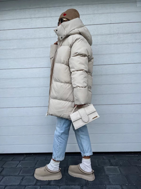 Damen Winterjacke in Creme, gesteppt, mit Kapuze. Kombiniert mit blauer Jeans, beiger Mütze und Tasche. Modetrend, warm, stilvoll.