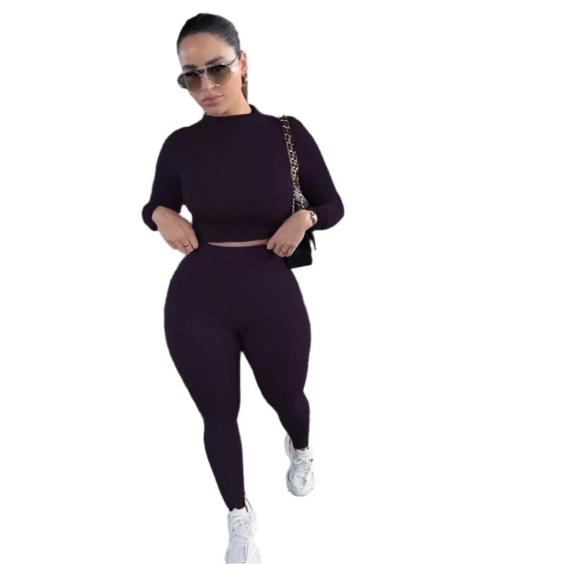 Frau in violettem Sportset, bestehend aus langärmligem Oberteil und Leggings, trägt Sonnenbrille und weiße Sneaker. Fitnessmode, Damenbekleidung.