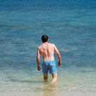 Mann in blauer Badehose aus recyceltem Polyester am Strand, Meer im Hintergrund. Nachhaltige Bademode, umweltfreundlich, Sommermode.