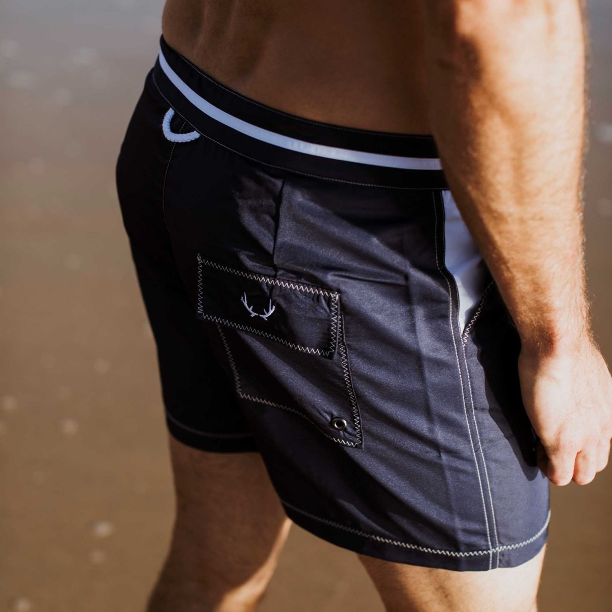 Marineblaue Herren-Badeshorts aus recyceltem Polyester mit orangefarbenen Details, ideal für nachhaltige Mode und Strandaktivitäten.