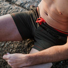 Khaki Badeshorts für Herren aus recyceltem Polyester mit roten Details. Ideal für Strand und Sport. Nachhaltige Herrenmode, umweltfreundlich.