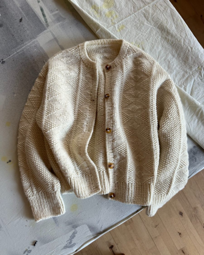 Handgestrickte Strickjacke aus Wolle in Cremeweiß mit Knopfleiste, Zopfmuster und Rundhalsausschnitt. Perfekt für Herbstmode und gemütliche Outfits.