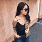 Frau in schwarzem Top und blauer Jeans, trägt beige Daunenjacke und Sonnenbrille. Modetrend, lässiger Stil, Streetwear, Herbstmode.