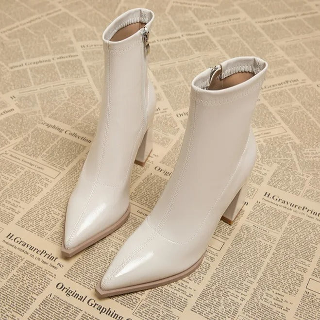 Elegante weiße Stiefeletten mit spitzem Absatz auf Zeitungshintergrund. Modische Damenstiefel, ideal für Herbstmode und stilvolle Outfits.