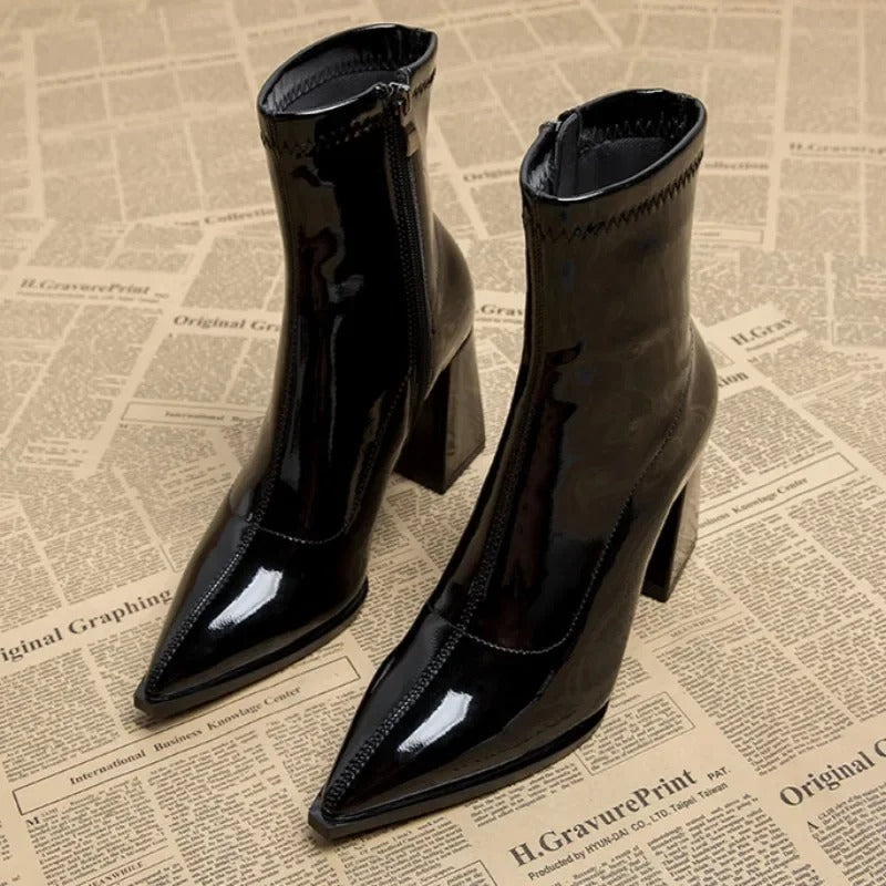 Schwarze Lackleder-Stiefeletten mit spitzem Absatz auf Zeitungshintergrund. Modische Damenstiefel, ideal für Herbst und Winter.