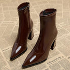 Braune Lackleder-Stiefeletten mit Blockabsatz und spitzer Zehenpartie auf Zeitungshintergrund. Modische Damenstiefel, elegant und trendig.