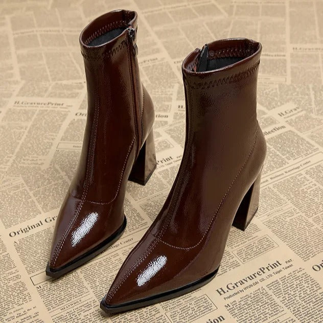 Braune Lackleder-Stiefeletten mit Blockabsatz und spitzer Zehenpartie auf Zeitungshintergrund. Modische Damenstiefel, elegant und trendig.