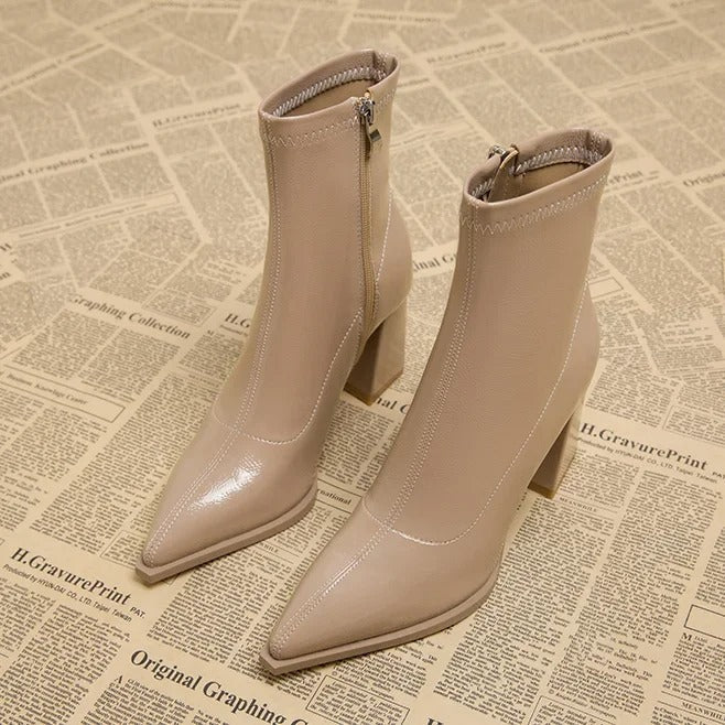 Beige Stiefeletten mit spitzem Absatz, Reißverschluss und Blockabsatz auf Vintage-Zeitungshintergrund. Modische Damenstiefel für Herbst/Winter.