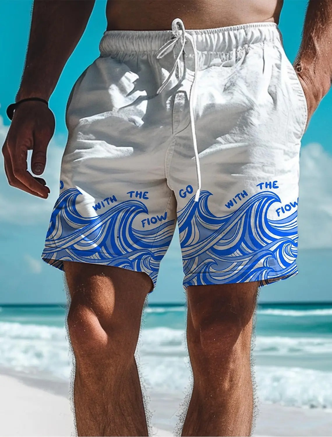 Weiße Badeshorts mit blauem Wellenmuster und Schriftzug "Go with the flow" am Strand.